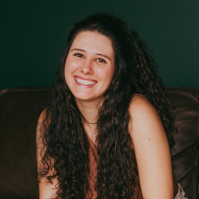 Julia Kalil sorrindo, sentada num sofá de couro